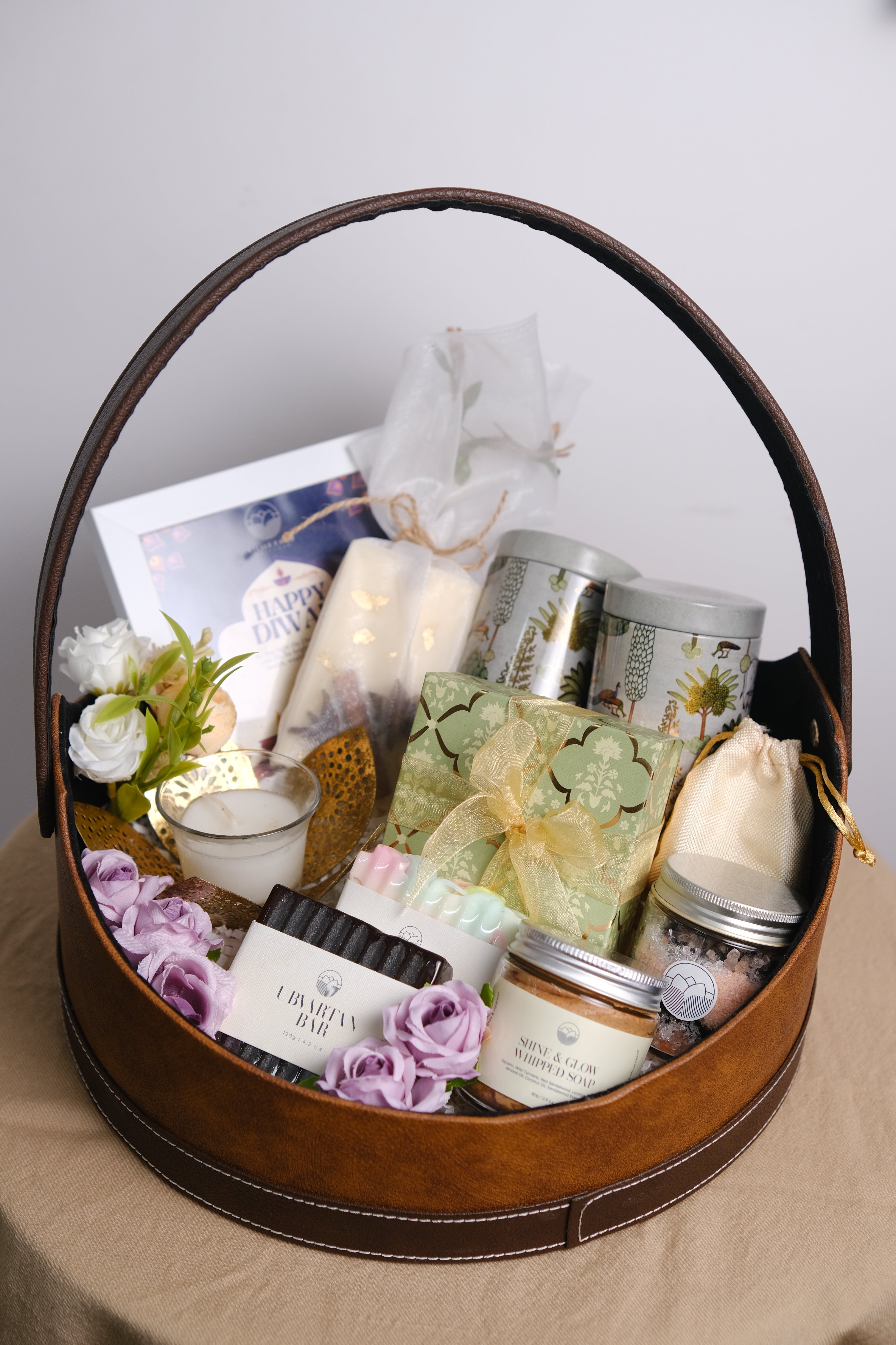 Round wooden box with decorative items including candles, flowers, and a book on a light background